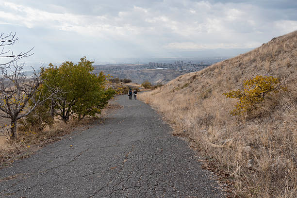 Two unrecognizable persons hiking in hills at autumn day enjoying Amazing View to Yerevan city of Armenia