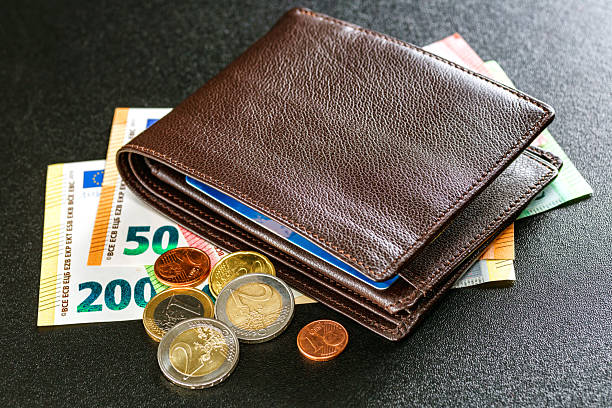 A shiny two euro coin placed next to a women’s wallet, close up detail.