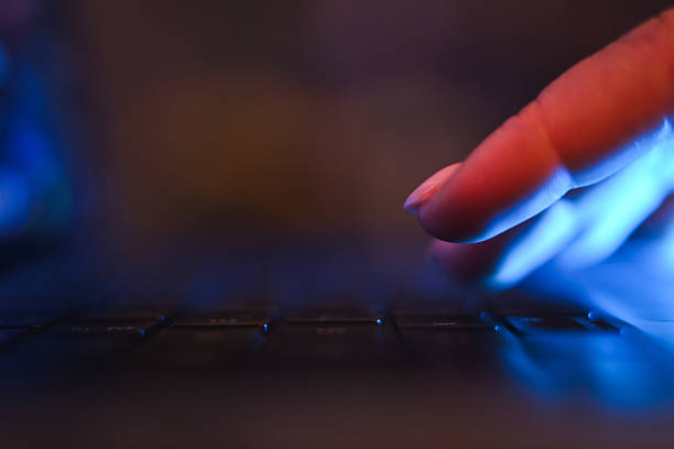 Hand typing on a laptop keyboard reflecting blue screen light in a dark environment