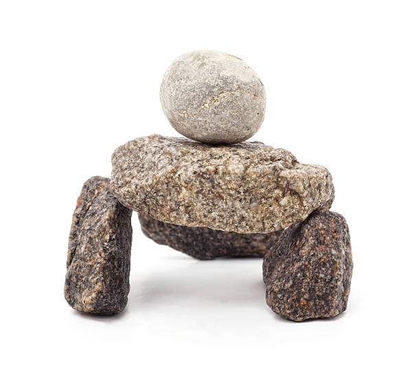 Arrangement of natural stones stacked into a small balanced sculpture on a white background. The composition features rough textured rocks forming a simple structure with a rounded stone placed on top, symbolizing balance.