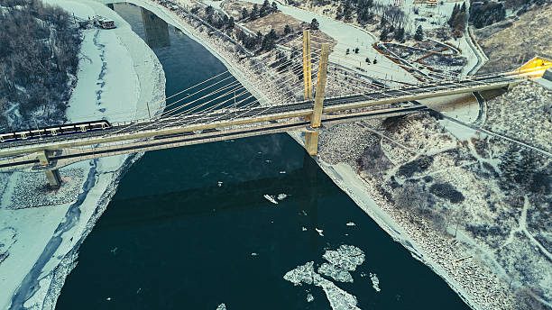 Aerial winter view of a bridge crossing the frozen North Saskatchewan River in Edmonton, captured at sunrise with soft light reflecting on snow and ice.