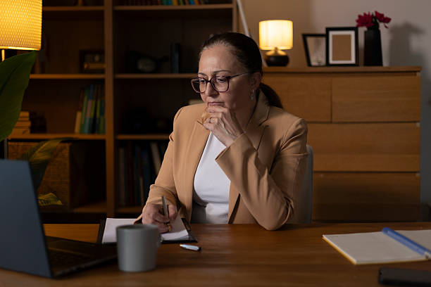 istock Woman working late, diligently taking notes and concentrating while sitting at her home office desk, surrounded by warm lamp light 2249222307