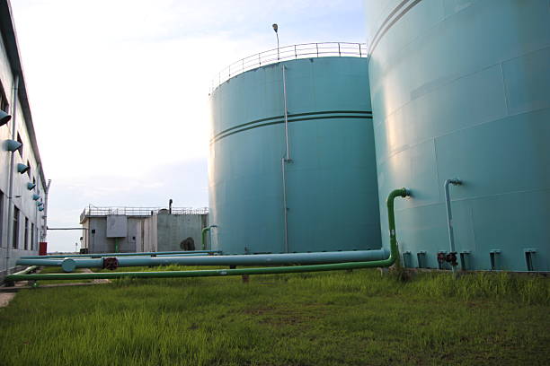 Industrial storage tanks with green pipes in facility grounds under bright sky during daytime.