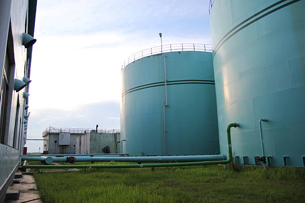 Industrial storage tanks stand tall on grassy field under a cloudy sky landscape view.