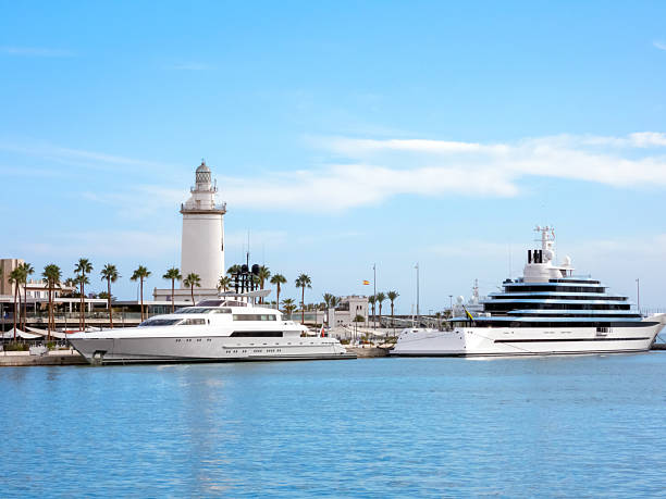 Malaga, Andalusia, Spain - September 21, 2025: Port of Malaga. A luxury yachts are anchored in a marina with a lighthouse nearby, surrounded by palm trees, evoking a peaceful coastal setting and a relaxed lifestyle.
