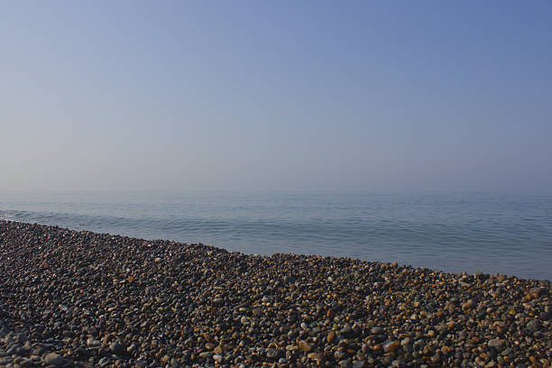 Minimalistic seascape with a stony pebble beach in the foreground and a calm sea under a clear blue sky. Empty tranquil coastal landscape with plenty of copy space, ideal as a background or panoramic banner.