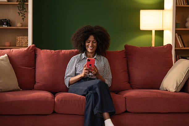 istock Young black woman using phone while sitting on cozy sofa at home 2249240165