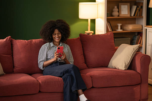istock Young black woman using phone while sitting on cozy sofa at home 2249240206