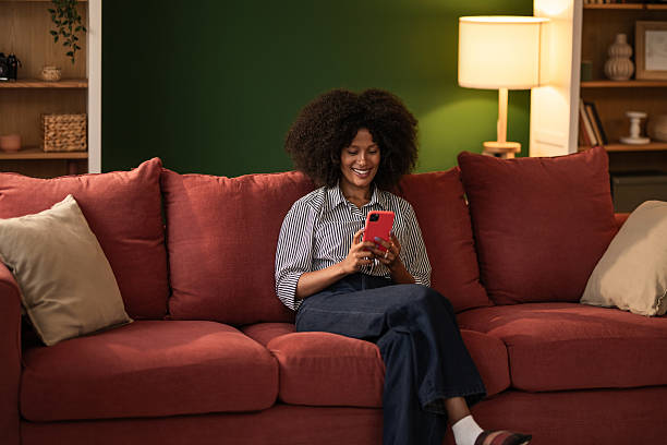 istock Young black woman using phone while sitting on cozy sofa at home 2249240219