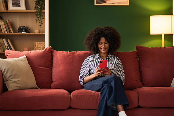 istock Young black woman using phone while sitting on cozy sofa at home 2249240250