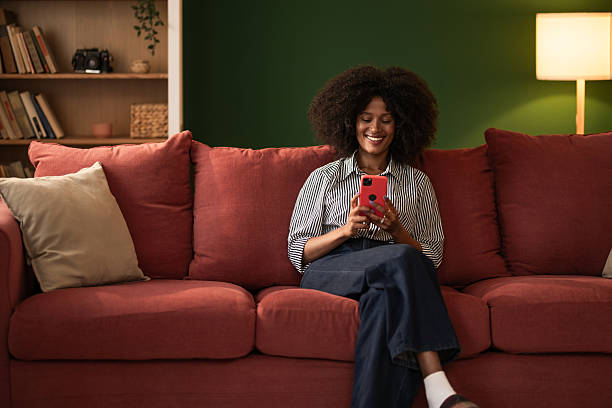 istock Young black woman using phone while sitting on cozy sofa at home 2249240806