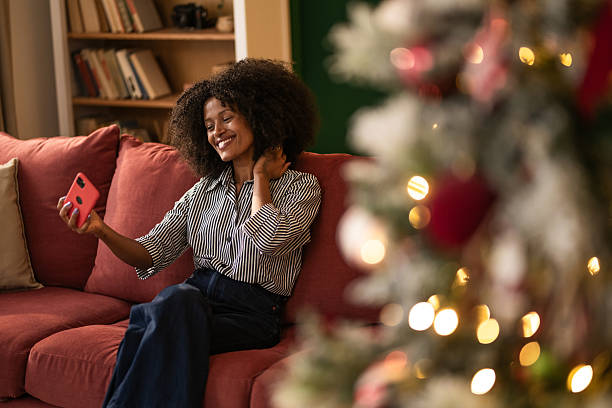 istock Young black woman taking a selfie while sitting on cozy sofa at home on Christmas 2249240943