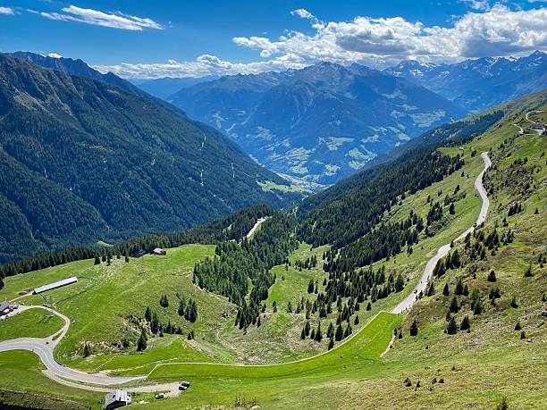 Panoramic view into Passeier Valley (germ. Passeiertal) from Jaufenpass in South Tyrol, Italy with winding mountain road, green pastures and forested slopes under a blue sky