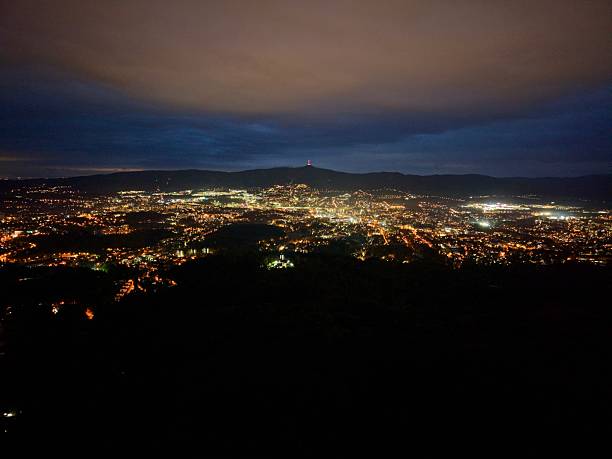 city lights spread across valley night, glowing like scattered constellations beneath low clouds winding