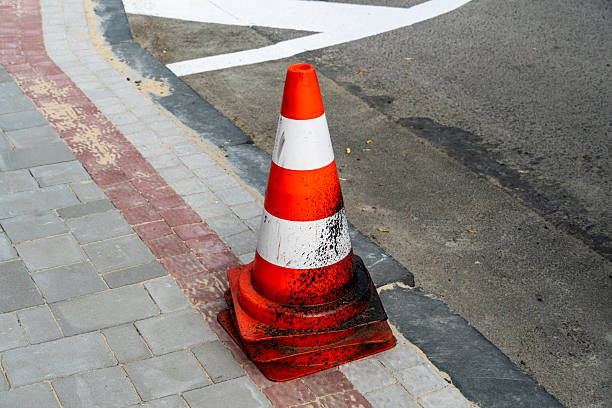 istock A single orange and white traffic cone rests on two stacked cones on a sidewalk next to an asphalt road, signaling caution. 2249254264