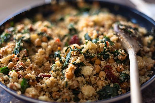 Close-up photograph of a bowl of couscous mixed with spinach, sun-dried tomatoes, and chickpeas