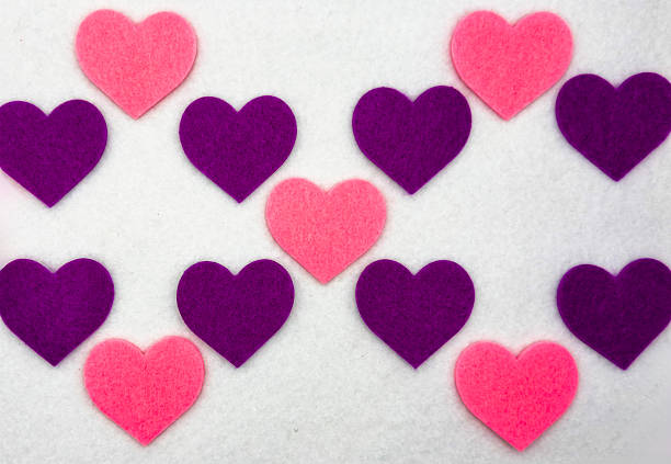Bright flat lay pattern featuring pink and purple felt hearts arranged in a repeating decorative layout on a clean white background. Soft handmade texture creates a romantic and playful atmosphere perfect for Valentine’s Day, love themes, greeting cards, wallpapers, and festive design projects.