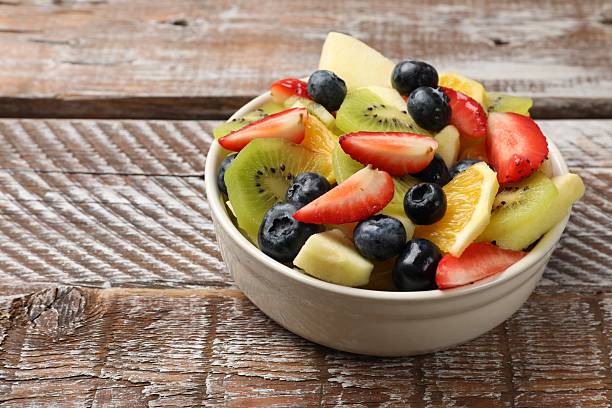 istock Tasty fruit salad in bowl on wooden table, closeup. Space for text 2249264641