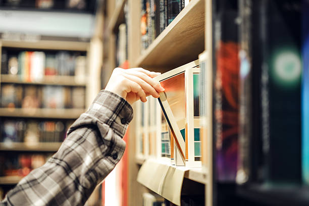 istock Hand pulling a book from bookstore shelf, choosing literature in cozy retail environment 2249266207