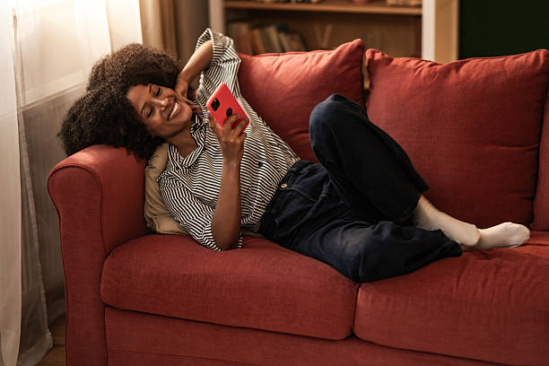 istock Happy black woman using phone on sofa at home. 2249273065