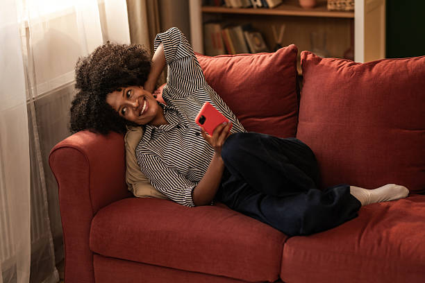 istock Happy black woman using phone on sofa at home. 2249273679