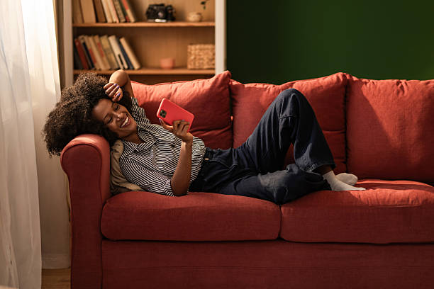 istock Happy black woman using phone on sofa at home. 2249273711