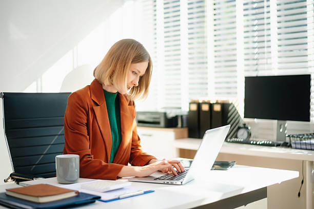 istock Focused business woman working on laptop in a bright modern office. Professional workspace, productivity, corporate job, technology, and career concept. 2249275874