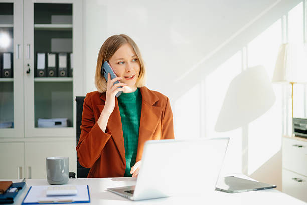 istock Professional woman on phone call in modern office, working on laptop. 2249275876
