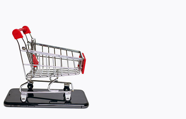 A small shopping cart stands on a mobile phone on a white background. The concept of online shopping using the phone. Convenience of remote purchases using modern technologies. Free space for text