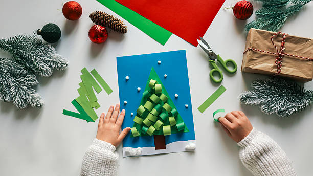 istock Child making a Christmas tree card with paper and decorations on a white table 2249277866