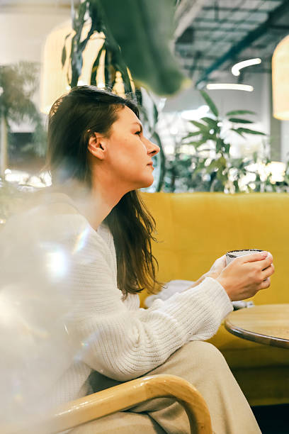 istock Woman relaxing with a warm drink in a cozy modern cafe surrounded by soft light and greenery 2249278544