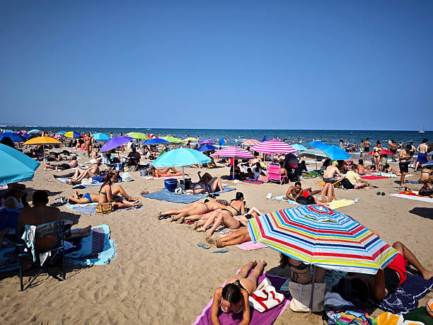 Crowd of people on Bondi Beach in the Eastern Suburbs of Sydney on Sunday, 8 January 2023.  The red and yellow coloured uniform of a lifesaver is visible on the top right edge.   This image was taken at the southern end of the beach looking north in the early afternoon.