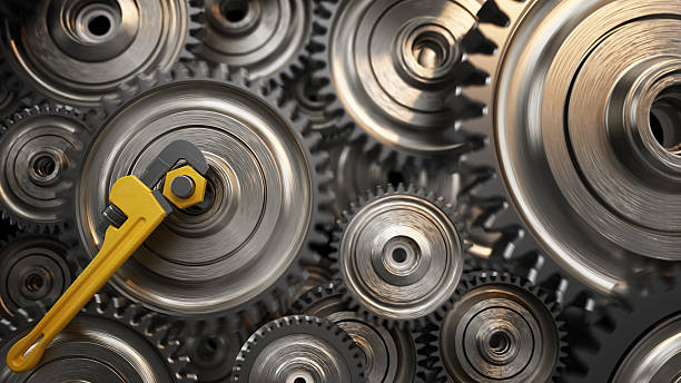 A collection of shiny metallic gears is arranged closely together, with a yellow adjustable wrench positioned on a yellow small gear. Leadership concept.