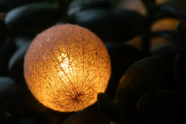 Close-up of a single warm, glowing cotton ball from a holiday garland. The festive light sits on a dark green plant, creating a cozy and magical mood.