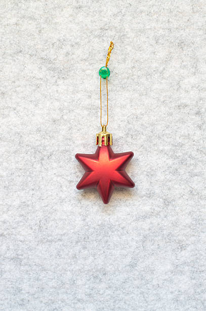 One cute beautiful three dimensional 3D shiny star shape Christmas ornament hanging with thumbtack pin by golden thread, string over furry gray white background bulletin board in the middle centre for celebration greeting cards, posters, backdrops.