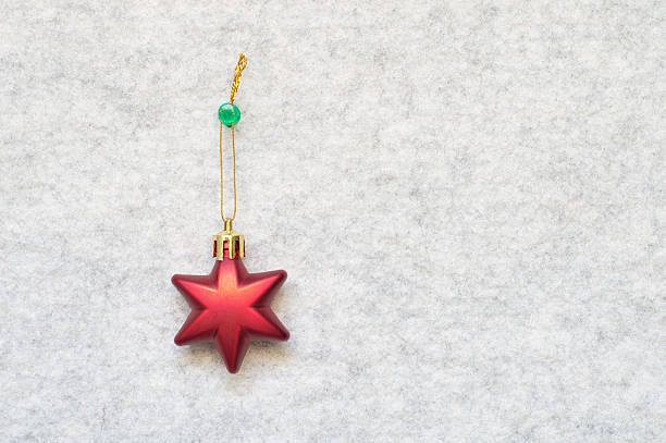 One cute three dimensional 3D shiny star shape Christmas ornament hanging with thumbtack pin by golden thread, string over furry gray white background bulletin board with copy space for celebration greeting cards, posters, backdrops.