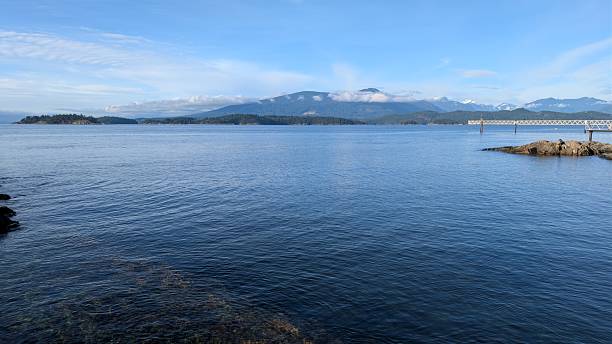 istock Tranquil Scenic Seascape with Rocky Shoreline, Coastal Pier, Forested Islands, and Distant Mountains 2249286191