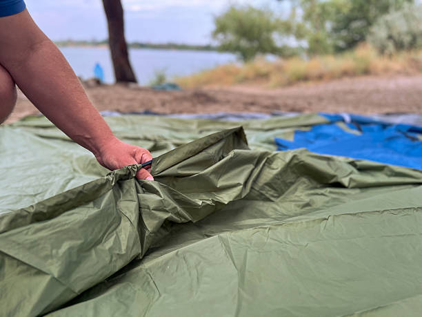 Adult hand pulling tent fabric, setting up camp by a lake under cloudy sky