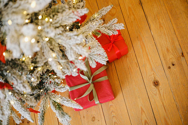 istock Flocked Christmas tree with warm lights and red gift boxes on a wooden floor 2249288333