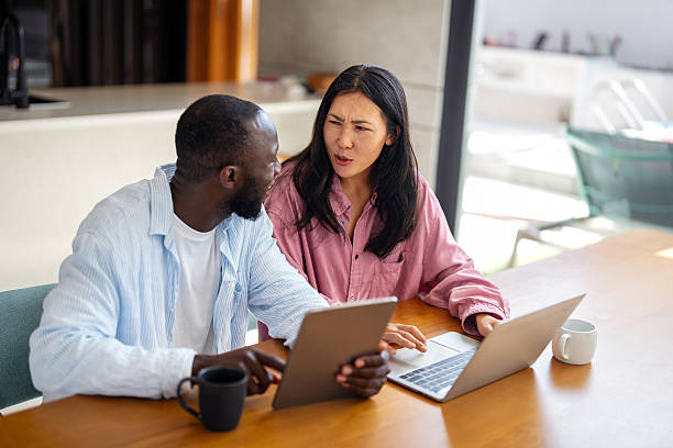 istock Multinational couple enjoying their morning routine, smiling and using laptop and tablet at home 2249289194