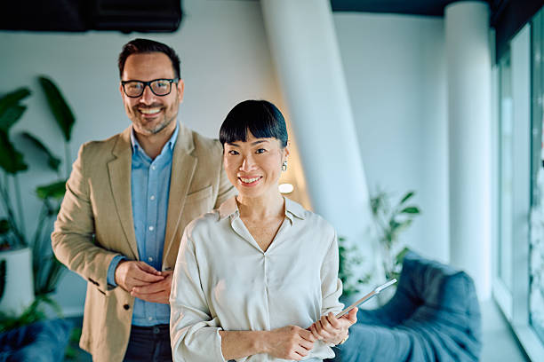 istock Business colleagues standing in modern office, smiling for camera and holding digital tablet, collaborating on project 2249293179