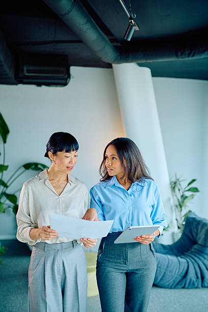 Businesswomen collaborating, discussing documents, and using digital tablet in a modern office, focusing on teamwork and strategy