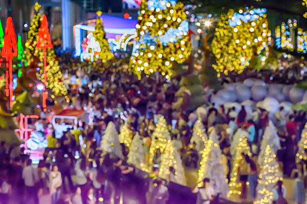 A festive crowd gathering in a plaza with glowing Christmas trees and decorations all around.