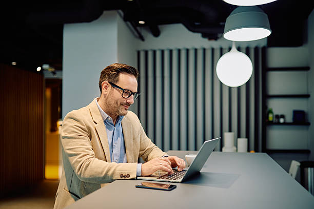 istock Businessman working remotely on laptop, typing on keyboard inside modern office workspace, focusing on screen 2249295175