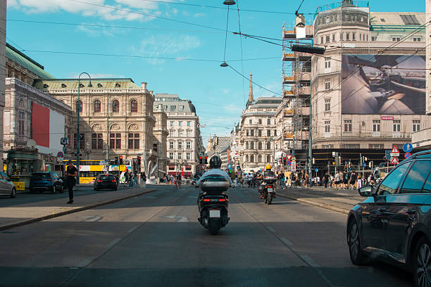 A wide-angle view captures motorbikes, cars, and pedestrians within the bustling urban streets, showing the surrounding cityscape and environment in full context.