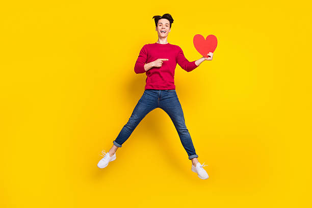 istock Full length photo of excited cute young guy dressed red pullover pointing finger red heart jumping isolated yellow color background 2249298726