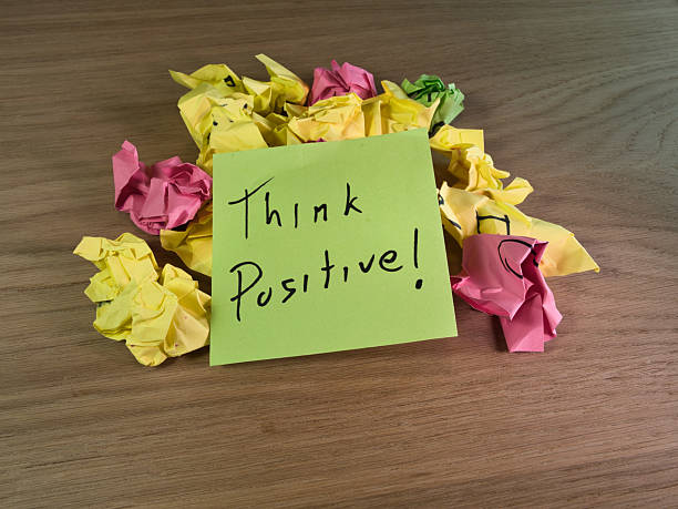 istock Think Positive Note on Crumpled Paper - An inspirational sticky note Think Positive! sits atop a pile of colorful crumpled papers on a wooden desk, symbolizing overcoming challenges. 2249300567