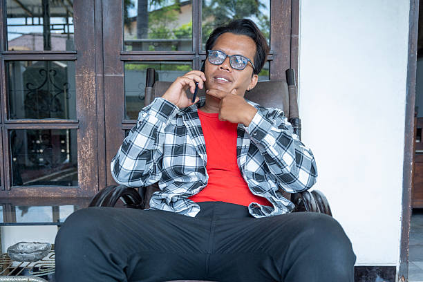 Indonesian southeast asian man relaxing on a chair outdoors while talking on his cellphone