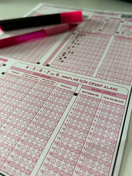 istock Student taking exams, writing examination on paper answer sheet optical form of standardized test on desk doing final exam in classroom, Education assessment Concept. 2249303092