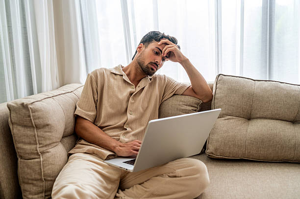 istock Relaxed Man Working On Laptop At Home Looking Thoughtful And Stressed On Couch 2249303358
